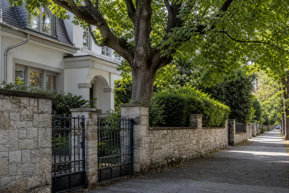 Gepflegtes Haus hinter klarer Grundstücksgrenze und altem Baum.
